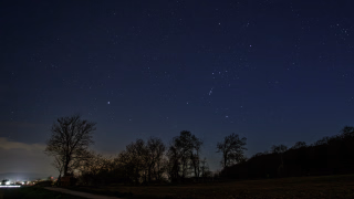 Nachthimmel über dem Benther Berg. Sirius und Orion stehen im Süden. Bäume im Vordergrund und die Lichter von Gehrden am Horizont.