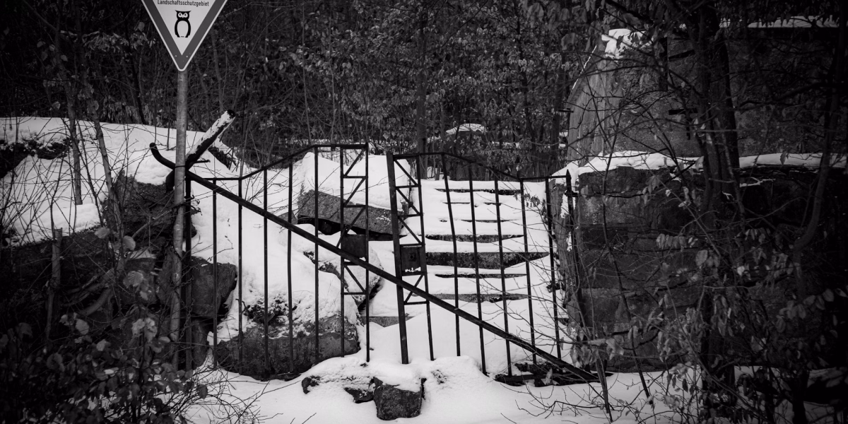 Das alte Eingangsportal vom Benther Berg Gasthaus. Verfallene Mauern und Treppen. Schnee auf den Stufen. Das alte Eisentor verrammelt mit einem Eisenrohr. Davor ein Schild Landschaftsschutzgebiet.